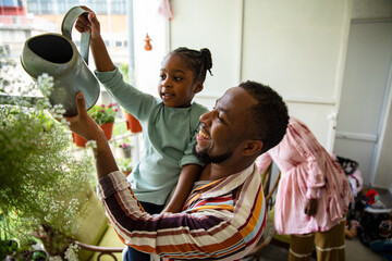 Little daughter watering plants with father