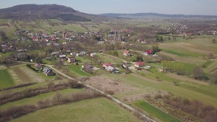Fototapeta na wymiar Cieklin, Poland - 4 9 2019: Panorama of a small European village with a Christian Catholic church in the center. Farms among green picturesque hills. Panorama of the Carpathian region with a drone