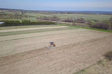 A farmer on a tractor with a seeder sows grain in plowed land in a private field in the village area. Mechanization of spring field work. Farmer's everyday life. Processing of land. The agrarian