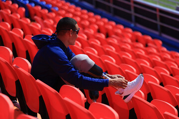 Asian man with a prosthetic running blade sitting on stadium bleachers