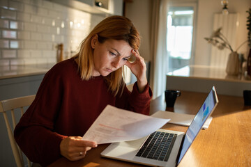 Woman Reviewing Documents at Home with Laptop on Kitchen Counter