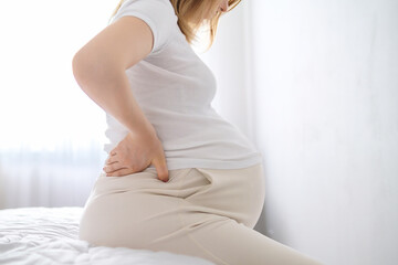 Pregnant woman sitting on the edge of the bed and holding her back.