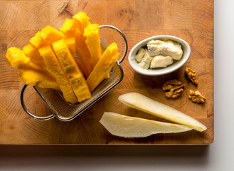 wooden cutting board with sticks of polenta, pear, nuts and cheese
