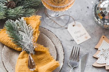 Table setting. Stylish plates, napkin, glass, champagne, Christmas tree branches and Christmas decorations on a gray background. The concept of merry Christmas and New Year 2024.