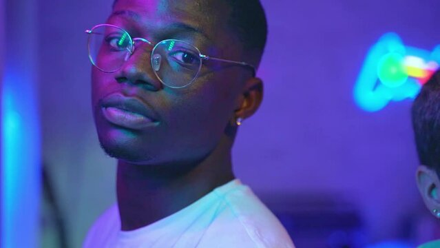 Portrait of handsome young black man looking at camera in room with neon light. High quality 4k footage
