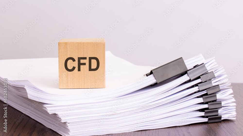 Poster a wooden block with a text cfd on a stack of paper documents. brown table, white background