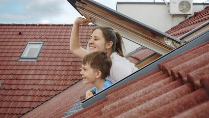 Happiness of a mother and her son as they open attic windows and peer outdoors, symbolizing the...