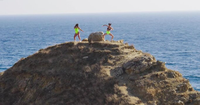 Slow motion of young adult women in swimsuits dancing twerk on a hill against the backdrop of the sea. Youth culture and entertainment. Vacation and relaxation. Degradation and animal instincts