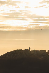 Man aged 25-29 standing on a seawall on the Atlantic Ocean in the yellow-orange rays of the sun near Oostende, Belgium