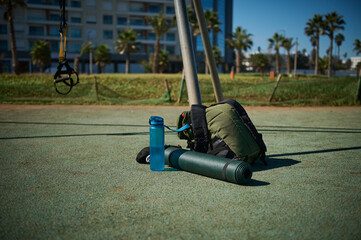Sports tools on the sports ground. A backpack, bottle of water and rolled fitness mat. Sport....