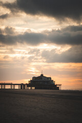 Obraz premium Sunset on the sandy beaches of Oostende, western Belgium. The last rays of the sun are breaking through the clouds. Red-orange hell