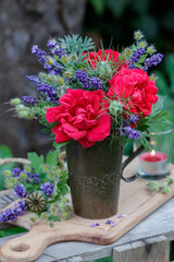 Blumenstrauß mit roten Rosen und Lavendelblüten im alten Kupferbecher im Garten