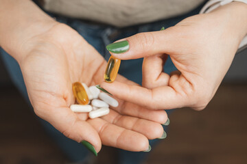Young woman takes one capsule of omega 3 supplement and holds pile of various medical pills and capsules in a hand, close-up view