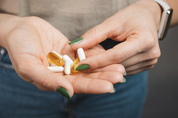 Young woman takes one white medical pill and holds in a hand pile of various pills and capsules, close-up view