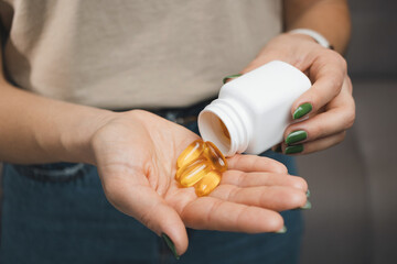 Young woman holds omega 3 capsules in a hand, female takes fish oil supplements and vitamins from a bottle, close-up view