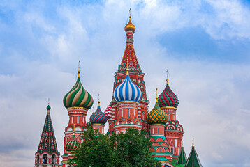 Fototapeta na wymiar Moscow, Russia - August, 25, 2010: Saint Basil Cathedral. Focus on its colorful towers wiht onion shaped domes on top against blue cloudscape. Some green foliage peeps in frontThe towers of the church