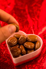 Man taking candy from heart shaped pot on red background 
