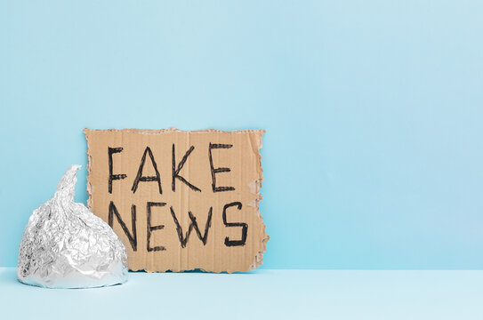 Aluminium foil hat and fake news poster on blue background, symbol for conspiracy theory and mind control protection. Top view. Space for text.