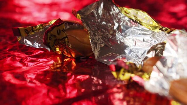 Man taking candy from its golden wrapper on red background