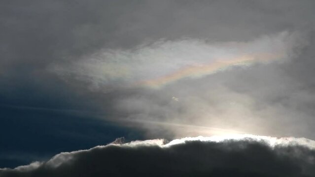 Natural sky background with moving dark and colorful cloud Iridescence, irisation - colorful pearl colors, optical phenomenon in cloud - and sunlight during mountain wind.