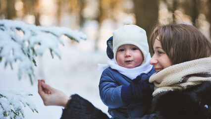 A mother shows her child a branch in a snow-covered forest. - obrazy, fototapety, plakaty