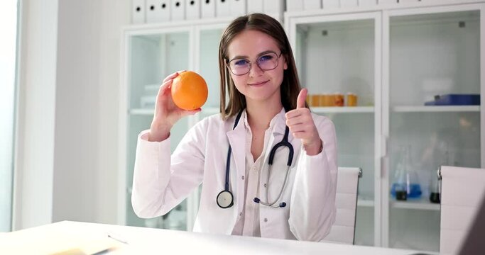 Dietitian doctor holds orange in hands and shows thumbs up gesture closeup. Healthy lifestyle and healthy vitamin diet