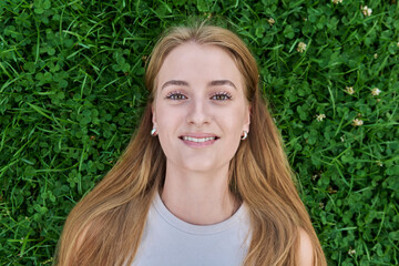 Top view, close-up of face of smiling blonde teenage girl lying on grass