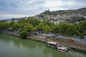 Fototapeta premium The Kura River running through Tbilisi, bridges and boats cruising on the river. 