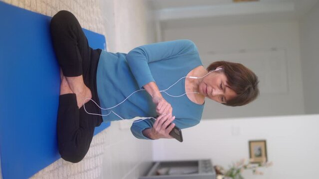 Middle age woman full-length yoga wearing ear buds listening to cell phone music