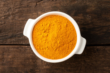 Turmeric powder in bowl on retro wooden background. Top view