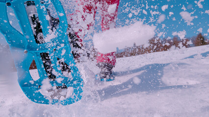 CLOSE UP, LOW ANGLE VIEW: Fresh snow flying behind lady running in snowshoes
