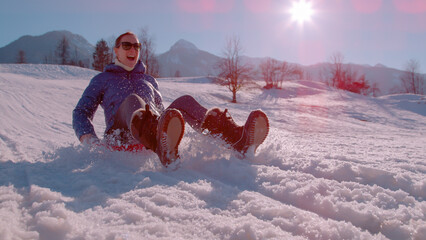 CLOSE UP, LENS FLARE: Sunny winter day with a lady sledding down the snowy hill