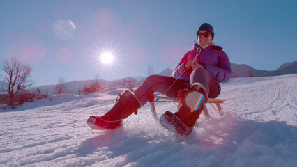 LENS FLARE, CLOSE UP: A beautiful lady is enjoying sledding with a wooden sled - obrazy, fototapety, plakaty