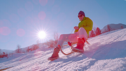 CLOSE UP, LENS FLARE: Active young guy enjoys a sleigh ride on winter holidays