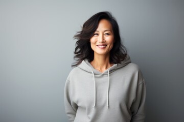 portrait of a beautiful asian middle age woman in hoodie sweatshirt isolated on light grey background