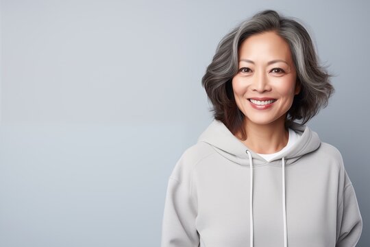 portrait of a beautiful asian middle age smiling woman in hoodie isolated on light grey background