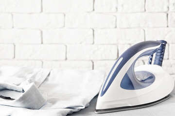 Modern electric iron and ironed shirt on the ironing board. Dressing and clothes theme