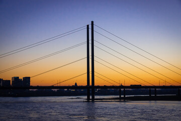 Fototapeta na wymiar Bridge over the river Rhine in Dusseldorf. It is sunset with orange light at the horizon and a blue sky.