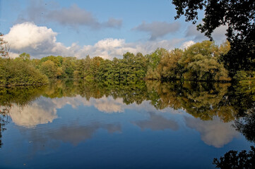 Bäume, Wolken und Himmel spiegeln sich in einem See 
Trees, clouds and sky are reflected in a lake