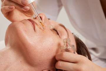 Close-up of the process of a beautician applying oil to a woman's face with a pipette Facial skin...