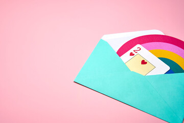 Blue love letter with a rainbow and a two of hearts card inside on pink background.