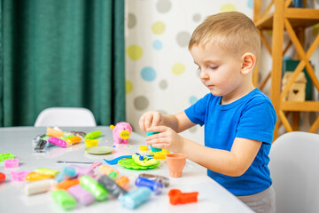 Little boy enthusiastically plays with plasticine, play dough on white table