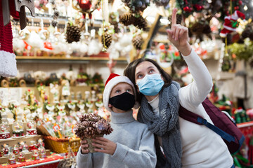 Tween boy with his mother wearing protective face masks looking for decorations on Christmas street market. Concept of protective measures to prevent COVID-19 transmission
