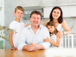 Middle-aged father, mother, preteen son and little daughter posing in the kitchen cheerfully