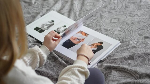 A teen girl flips through a photo book with photos of her dad and pregnant mom.