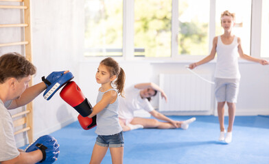 Father and girl engaged during training, boxing classes. Parent helps his daughter master basic...