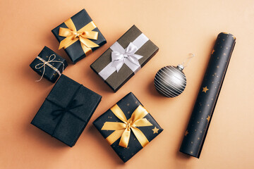 Christmas gifts in black boxes with golden and silver bows on beige background. Top view, flat lay