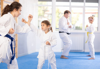 Parent with child partners during martial arts karate class train to perform basic blows to...