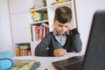 Distance learning online. A schoolboy boy studies at home. Child boy uses a laptop and communicates...