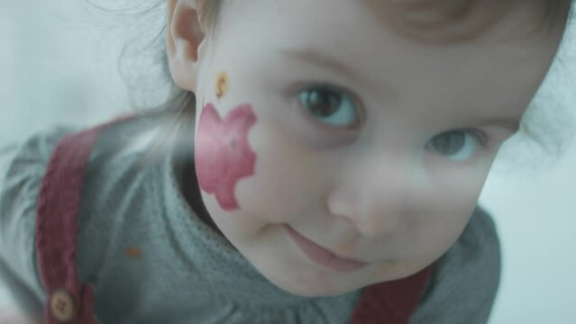 Cheerful toddler girl with a piggy bank painting on her face. Banking, financial education and deposit concept.